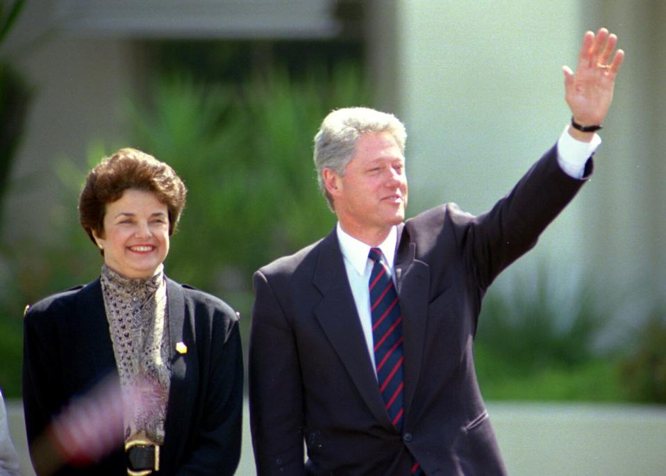 At right, Bill Clinton waves and California Sen. Dianne Feinstein stands at left, both smiling.