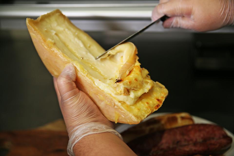 At restaurants and shops, half wheels of raclette are melted under a heating element. Then, as cheesemonger Mirella Barajas shows at West Allis Cheese and Sausage Shoppe at the Milwaukee Public Market, the melted cheese is scraped off to be eaten. Raclette's name comes from the French word racler, meaning to scrape.