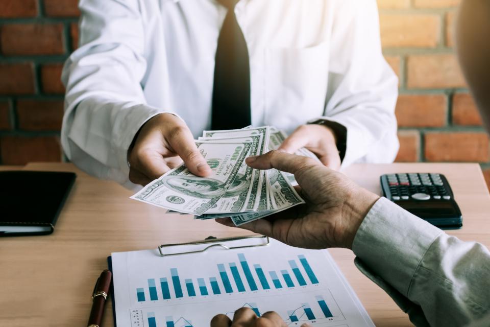 Man at a desk passing a handful of money to someone