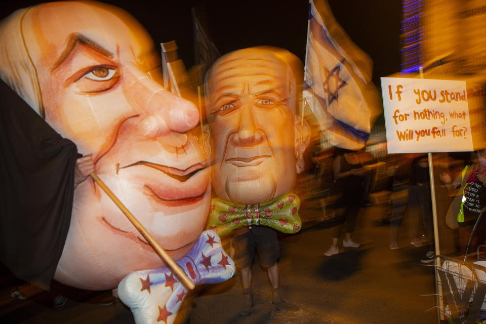 FILE - In this Saturday, Aug. 8, 2020 file photo, demonstrators wear mask depicting Israel's Prime Minister Benjamin Netanyahu, left, and Defense Minister and coalition partner Benny Gantz, right, during a protest in Jerusalem, Israel. When Netanyahu and his rival, Gantz, agreed to form an “emergency” government in May after three bitter, and ultimately deadlocked, election campaigns, the goal was to stabilize Israeli politics in the face of a global pandemic. Less than 100 days later their fractious coalition government appears to be headed toward collapse as Israel grapples with a raging coronavirus outbreak, an economic calamity and a wave of public protests. (AP Photo/Ariel Schalit, File)