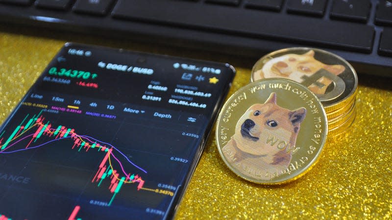 Gold Dogecoin coins sitting next to a phone displaying the price of DOGE over time.