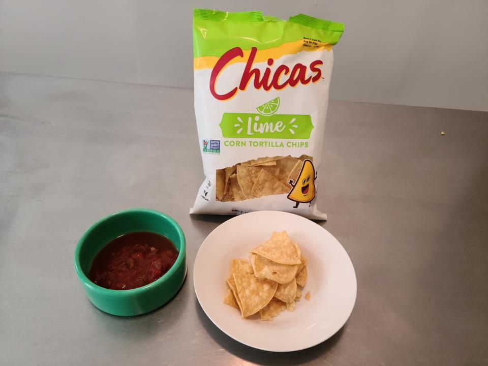 Bag of Chicas behind a plate of chips next to a bowl of salsa.