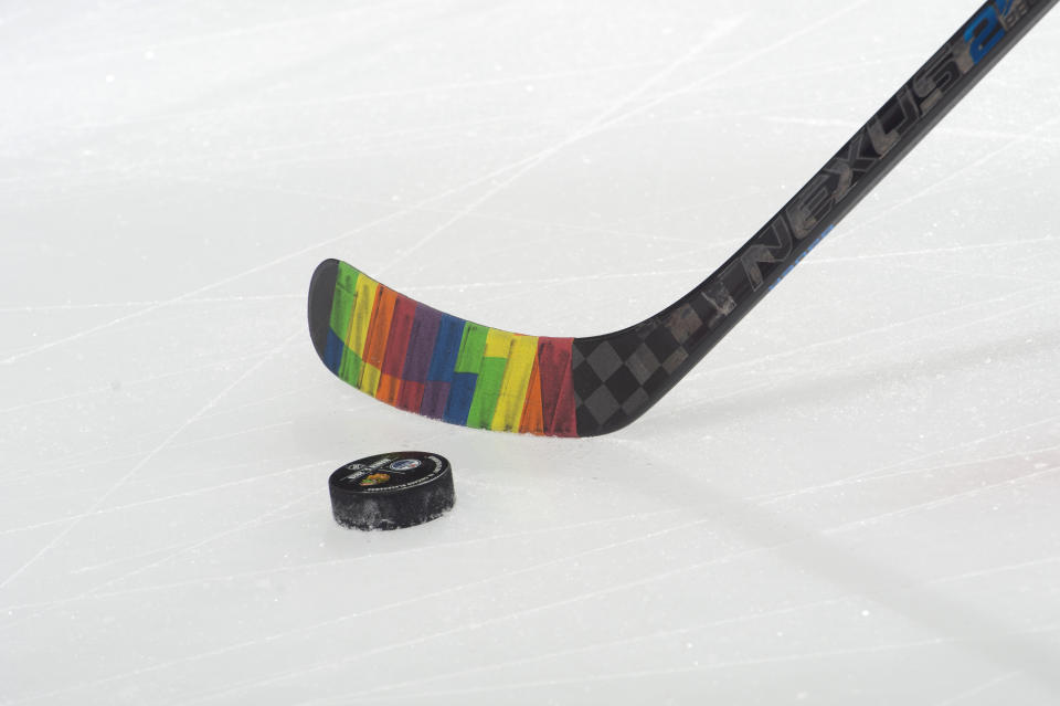 A hockey stick is taped in rainbow colors near a hockey puck.