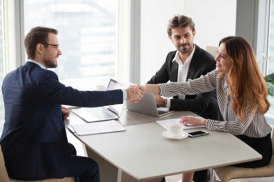 A man shakes hands with a woman across a desk.