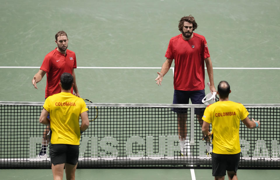 United States' Jack Sock, left, and his teammate Reilly Opelka salutes Colombia's Juan Sebastian Cabal and Robert Farah after their withdrawal during the Davis Cup men's doubles Finals tennis match at the Pala Alpitour in Turin, Italy, Sunday, Nov. 28, 2021. (AP Photo/Antonio Calanni)