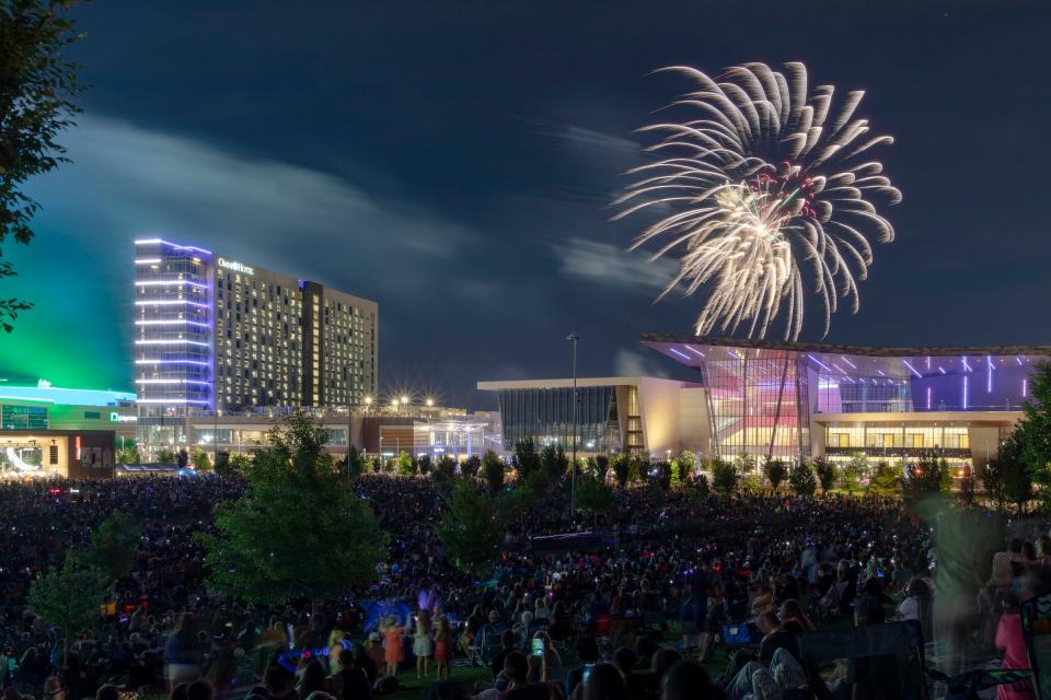 People watch fireworks at the end of the annual Oklahoma City Philharmonic Red, White, and Boom outdoor concert at Scissortail Park. The Omni Hotel is shown to the left of the convention center.