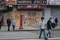 Volunteers Christian Tyler and Ashante West, right, carry brooms after participating in a community cleanup effort as they walk by a boarded up pawnbroker's store, Tuesday, June 2, 2020, in the Fordham Road area of the Bronx borough of New York. Protesters broke into stores Monday night in reaction to George Floyd's death while in police custody on May 25 in Minneapolis. (AP Photo/Mark Lennihan)