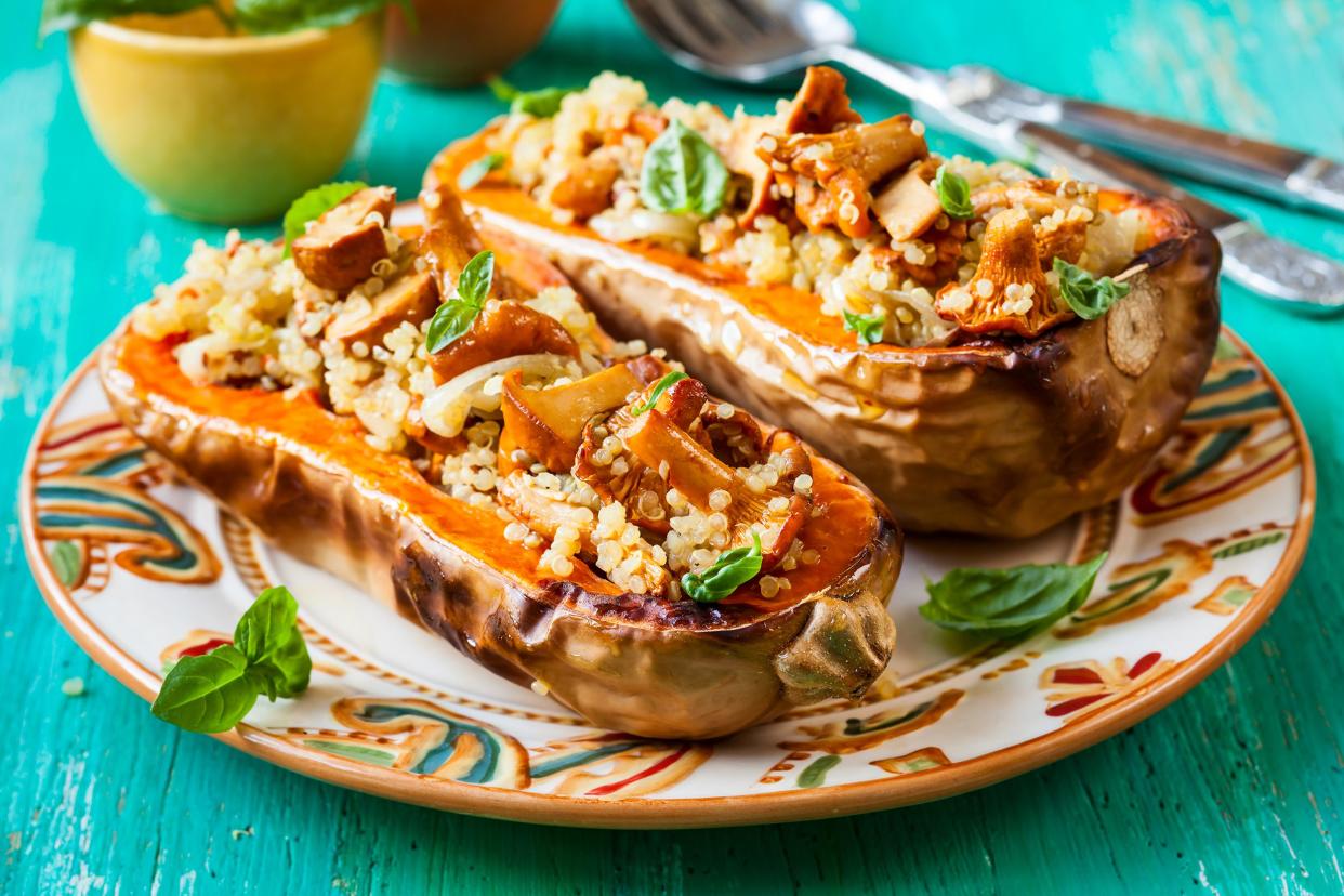 Stuffed roasted butternut squash on a southeastern style ceramic plate on a blue green table with utensils and food in the background