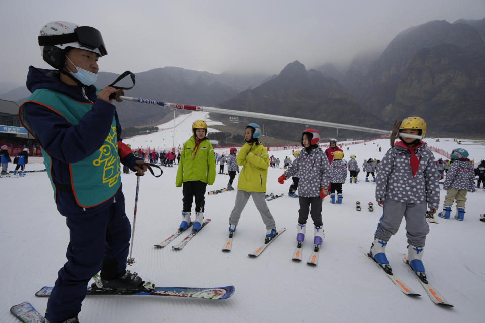A ski instructor points with a pole with school children taking ski lessons at the Vanke Shijinglong Ski Resort in Yanqing on the outskirts of Beijing, China, Thursday, Dec. 23, 2021. The Beijing Winter Olympics is tapping into and encouraging growing interest among Chinese in skiing, skating, hockey and other previously unfamiliar winter sports. It's also creating new business opportunities. (AP Photo/Ng Han Guan)