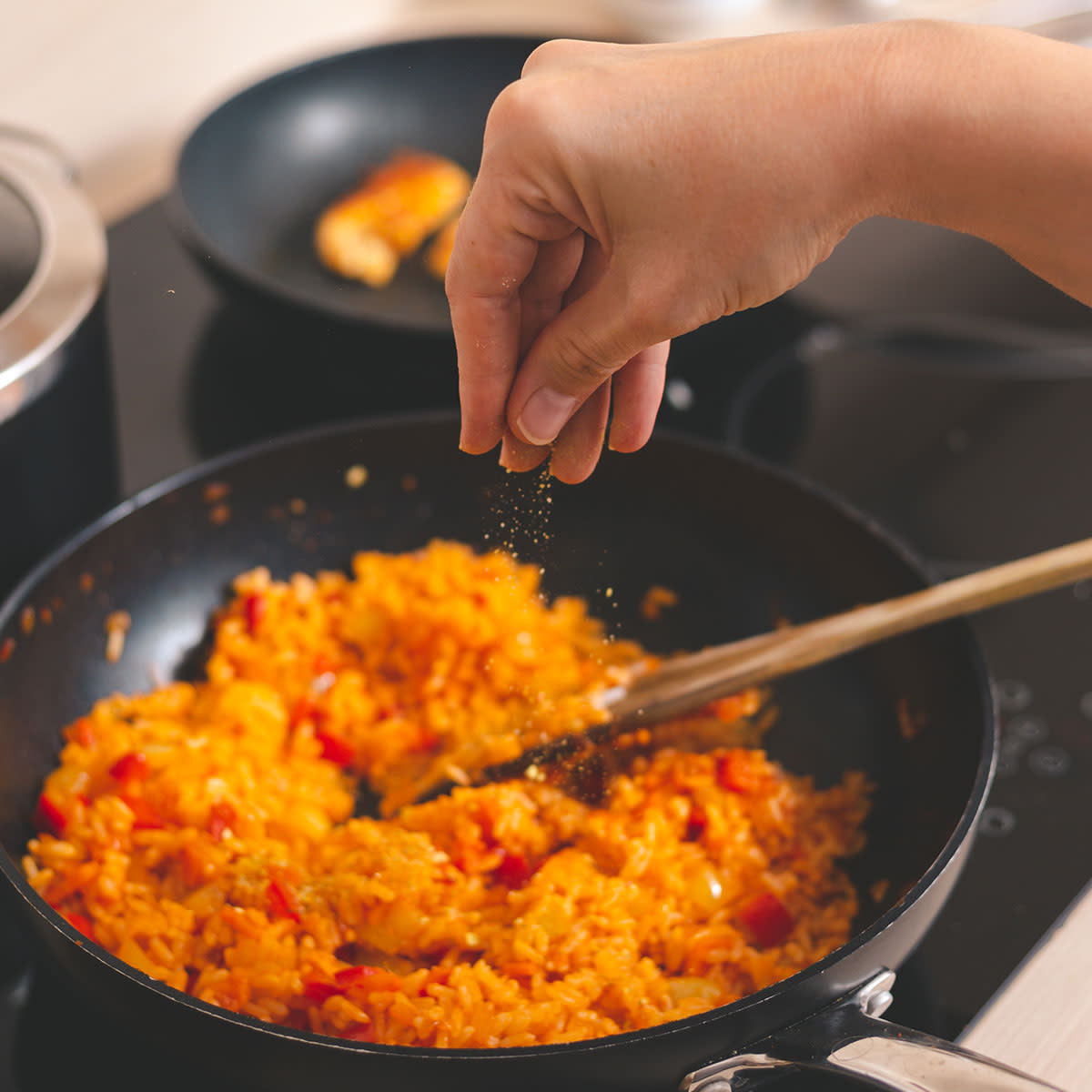 woman sprinkling spices into pan with food