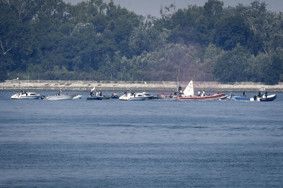 Environmentalists in small boats near the test site of a trial run of an anti-flood system of 78 inflatable barriers, wave protest banners as police speed boats cut their way, in Venice, Italy, Friday, July 10, 2020. Venice has conducted a trial run an ambitious anti-flood system of 78 inflatable barriers in the hopes of protecting the lagoon city from devastating high tides. Premier Giuseppe Conte on Friday at a ceremony in Venice pressed a button that activated compressors to pump air into the bright yellow barriers, which then started rising from the sea to act a kind of a dike-on-demand. (Claudio Furlan/LaPresse via AP)