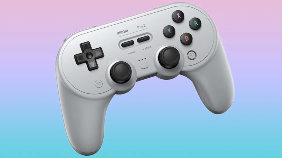 A grey gaming controller, similar to the PS1 style, is shown against a pastel rainbow background.