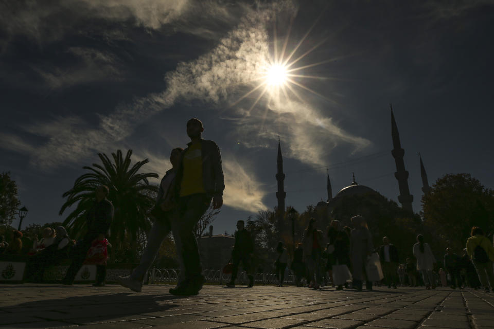 FILE - Pedestrians walk near Sultan Ahmed mosque during a partial solar eclipse in Istanbul, Turkey, Tuesday, Oct. 25, 2022. Throughout history, solar eclipses have had profound impact on adherents of various religions around the world. They were viewed as messages from God or spiritual forces, inducing emotions ranging from dread to wonder. (AP Photo/Emrah Gurel, File)