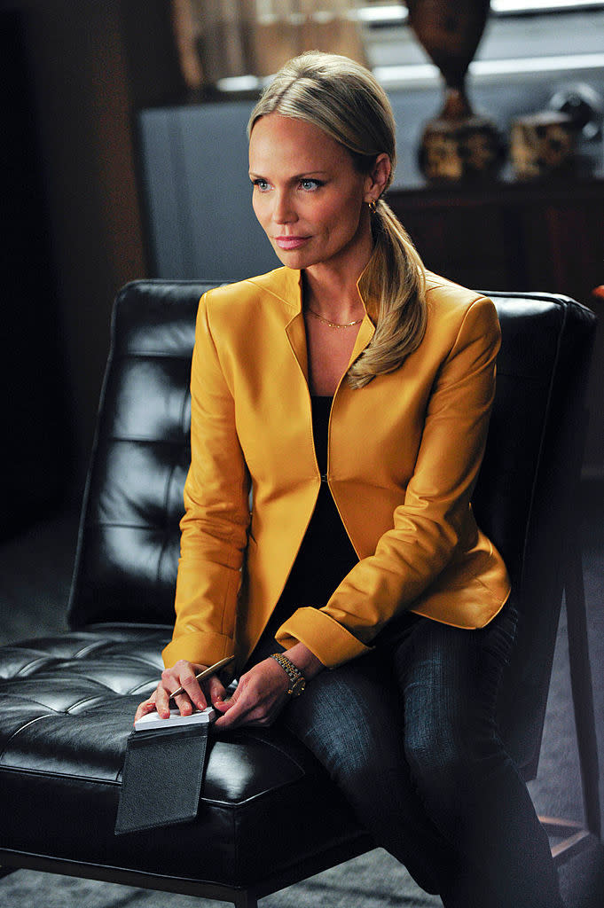 Kristin Chenoweth, wearing a tailored blazer and seated on a leather chair, looks engaged in a serious discussion in a scene