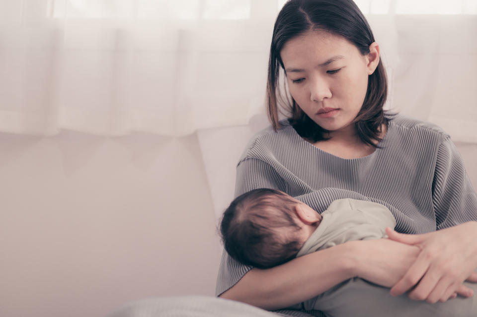 Mother Feeding Baby Boy While Sitting On Bed At Home