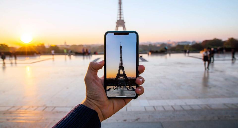 A man takes a photo on his phone of the Eiffel Tower in Paris.