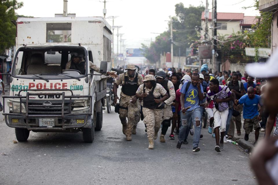 Police officers and protesters take cover behind a police truck as shots ring out during a protest to demand the resignation of Haiti's president Jovenel Moise on the 216th anniversary of Battle of Vertieres in Port-au-Prince, Haiti, Monday, Nov. 18, 2019. At least four people were shot and wounded during a small protest in Haiti’s capital after a speech by embattled President Jovenel Moise. A local journalist, a police officer and two protesters were rushed away with apparent bullet wounds. (AP Photo/Dieu Nalio Chery)