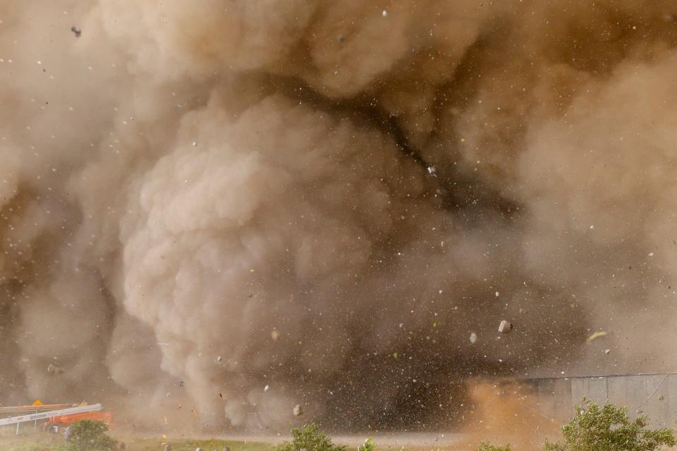 giant cloud of smoke with flying rocks and debris from starship rocket launch swallows equipment fencing in a lot with bushes