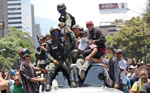 Soldiers ride on top of a car with supporters of Venezuelan opposition leader Juan Guaido during anti-goverment protests, in Caracas - Credit: CARLOS EDUARDO RAMIREZ/Reuters