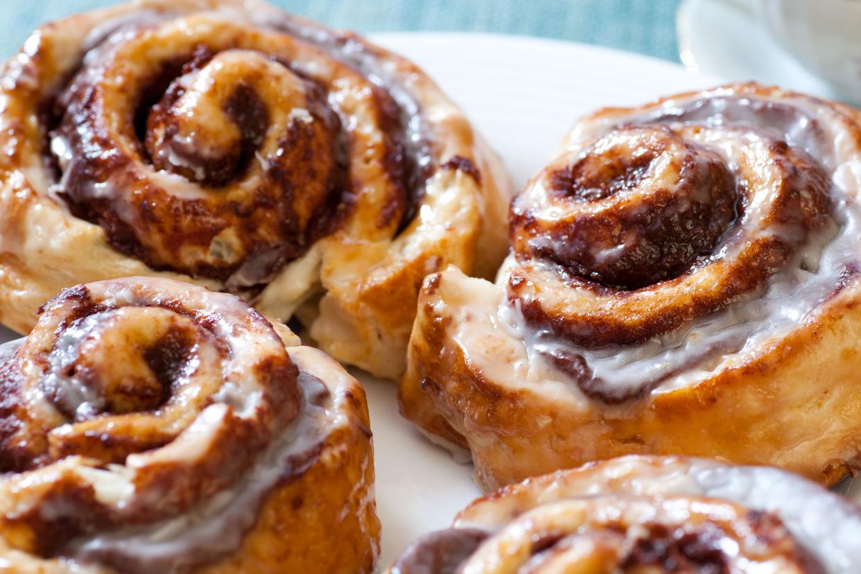 Closeup of four cinnamon swirl rolls on a white plate on a blue table and a knife in the background