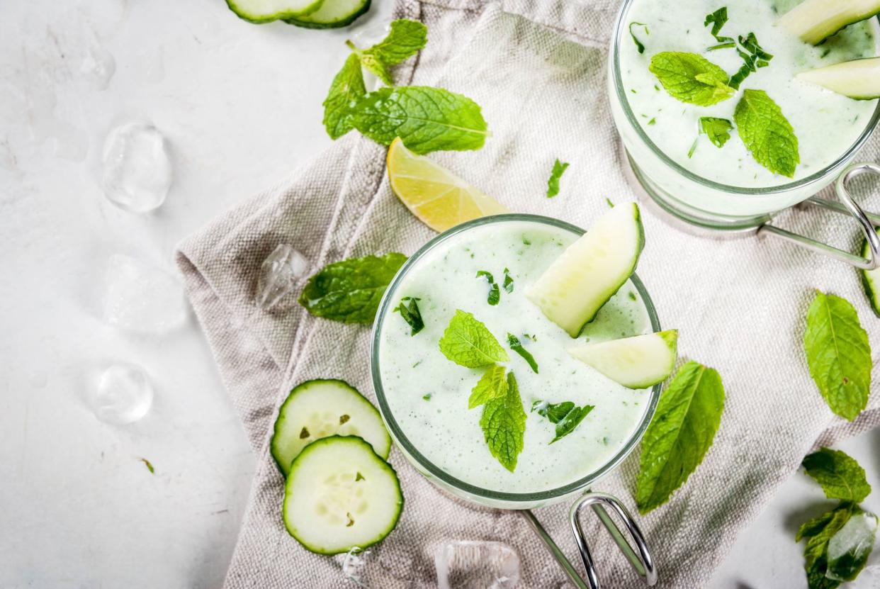 Summer food. Refreshing dishes. Cold soup of cucumber, avocado, with herbs and mint. With serving glasses, with slices of cucumber. On a white concrete table, with ingredients. Copy space top view