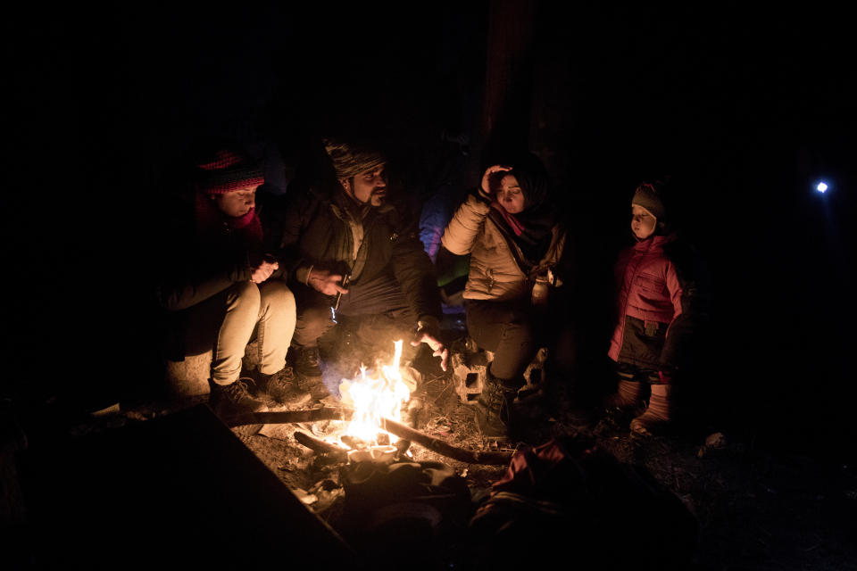 In this picture taken Thursday Dec. 12, 2019, Indian migrants Nishademi, 22, and Suhil, 23, warm up by a fire next to Fatma, 24, and her son Omar, 1, Syrian refugees form Aleppo, as they attempt to enter the EU through Croatia in the mountains surrounding the town of Bihac, northwestern Bosnia. (AP Photo/Manu Brabo)