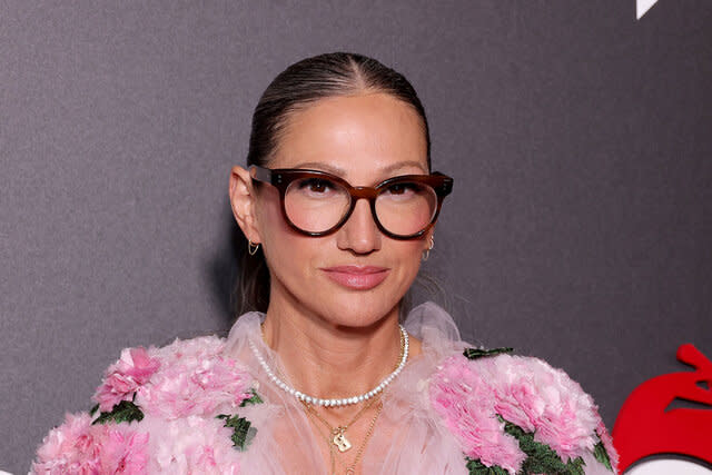 Jenna in a pink, floral, tulle top and thick, framed, eyeglasses and an updo.