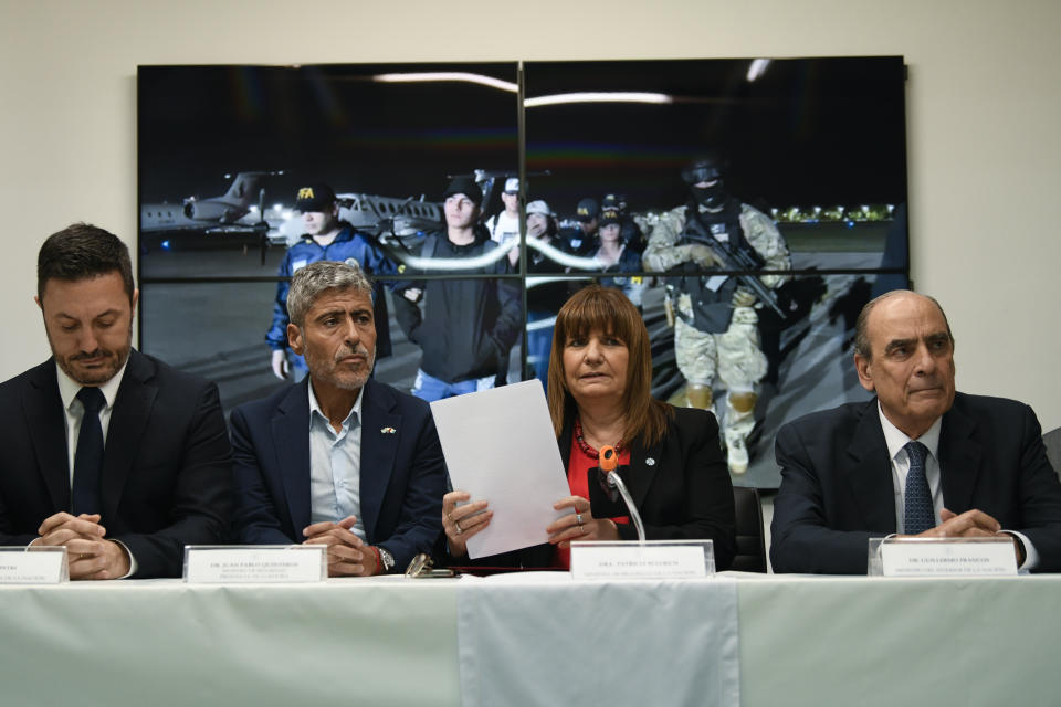 La ministra de Seguridad, Patricia Bullrich, segunda desde la derecha, el ministro de Defensa, Luis Petri, a la izquierda, el ministro de Seguridad de Córdoba, Juan Pablo Quinteros, segundo desde la izquierda, y el ministro del Interior, Guillermo Francos, a la derecha, dan una conferencia de prensa sobre la expulsión de la familia del prófugo narco ecuatoriano José Adolfo "Fito" Macías Villamar, mostrado en video detrás de ellos, en Buenos Aires, Argentina, el viernes 19 de enero de 2024. El líder de Los Choneros desapareció de una prisión de Guayaquil unas semanas antes. (Foto AP/Gustavo Garello)