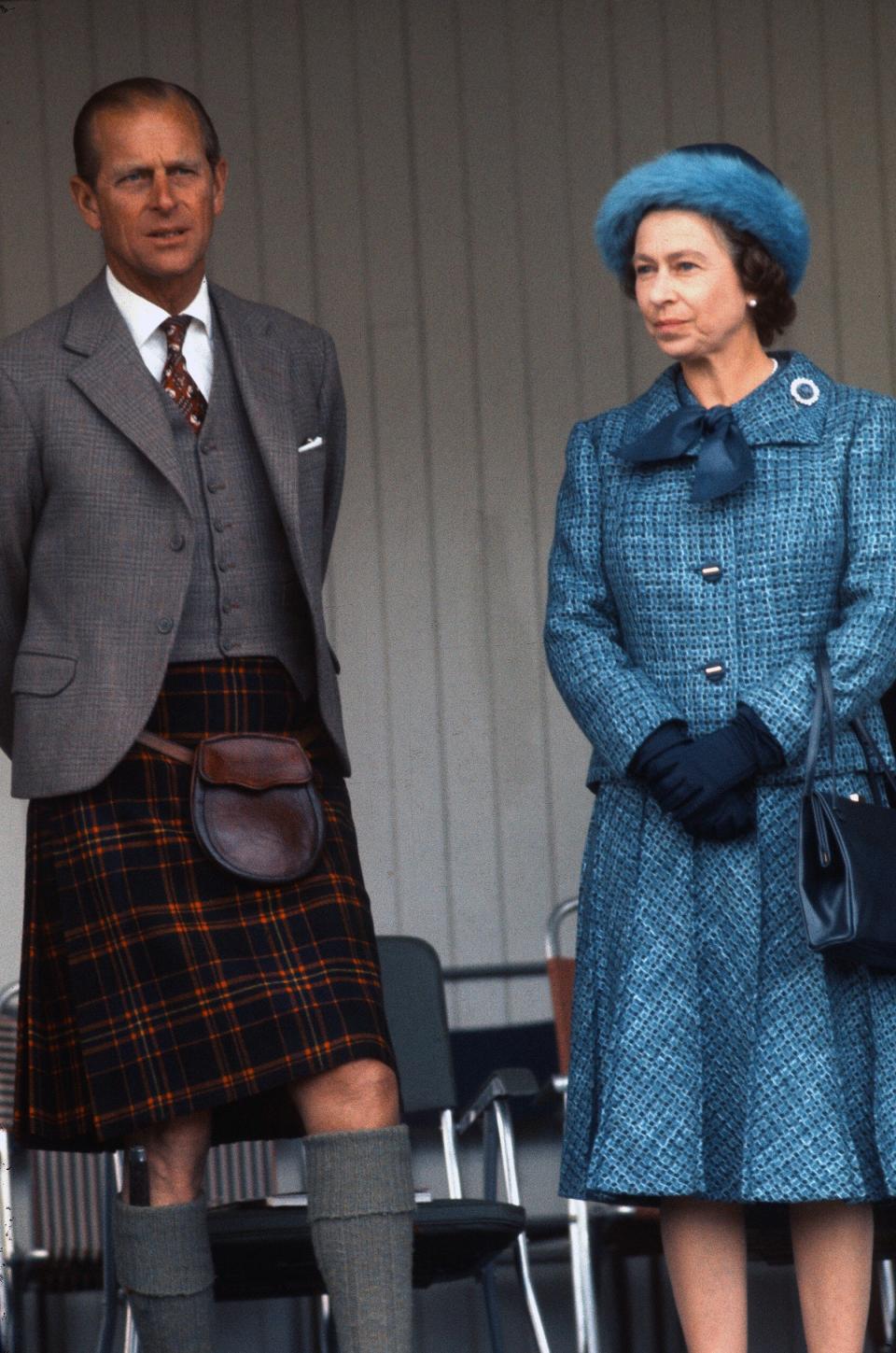 Prince Philip and Queen Elizabeth II, wearing a blue hat and coat dress, at the Braemar Highland Games in 1975.