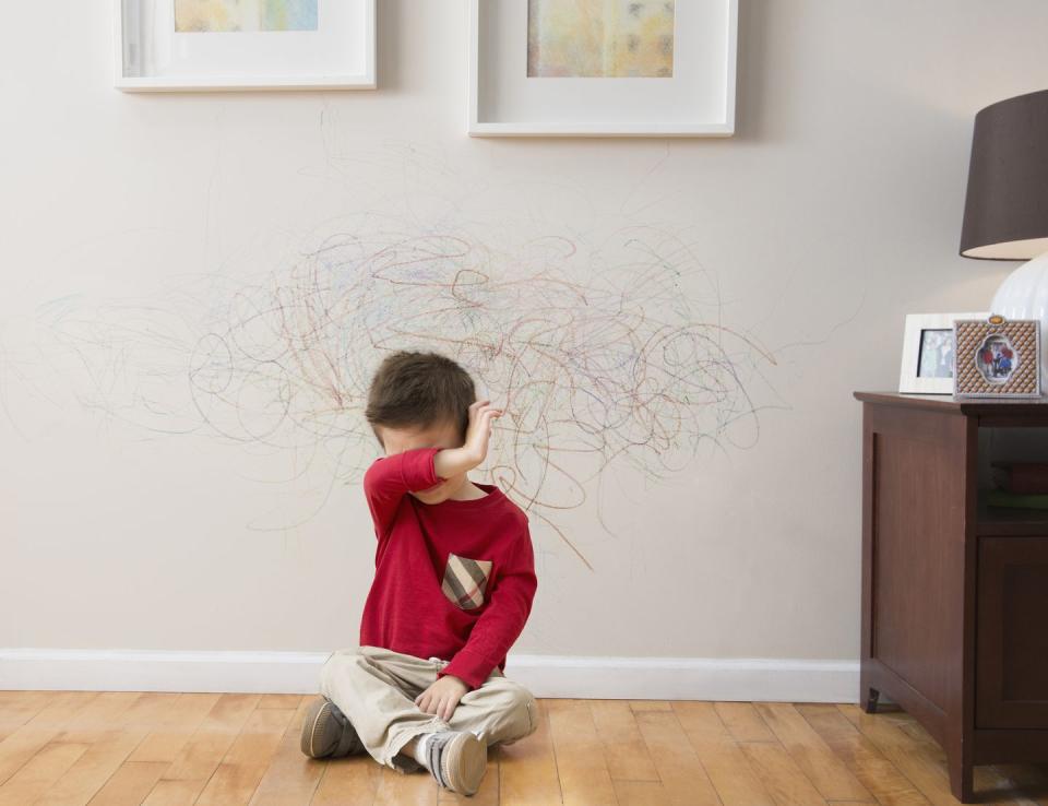 mixed race boy crying after drawing on wall with crayons