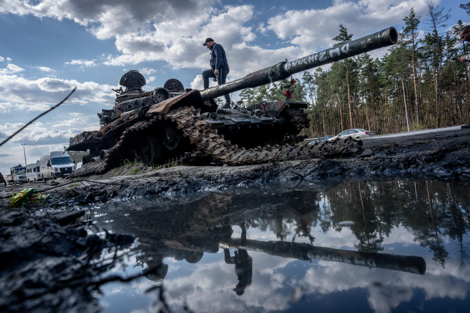 A man climbs over a destroyed Russian tank near a road.