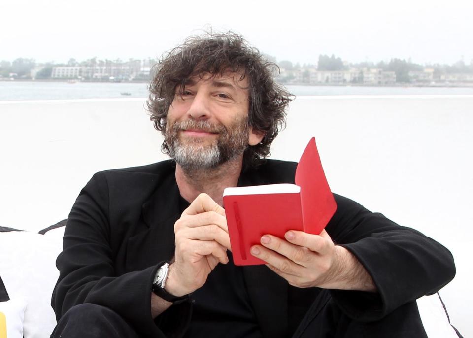 Neil Gaiman writing in a small red book on a yacht