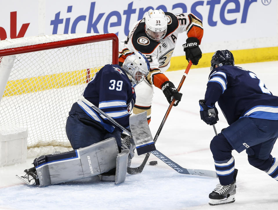 Winnipeg Jets goaltender Laurent Brossoit (39) saves a shot as Anaheim Ducks' Jakob Silfverberg (33) tries to jam it in the side and Jets' Dylan DeMelo (2) defends during second-period NHL hockey game action in Winnipeg, Manitoba, Friday, March 15, 2024. (John Woods/The Canadian Press via AP)