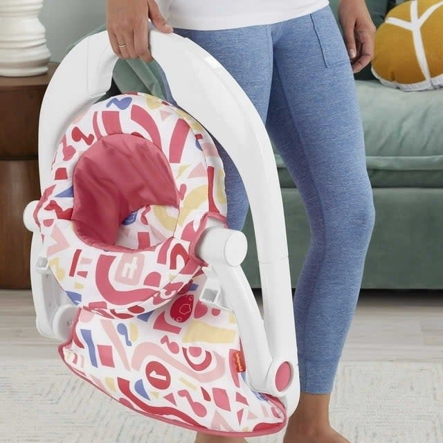 Person standing next to a baby's folded, colorful patterned bouncer chair