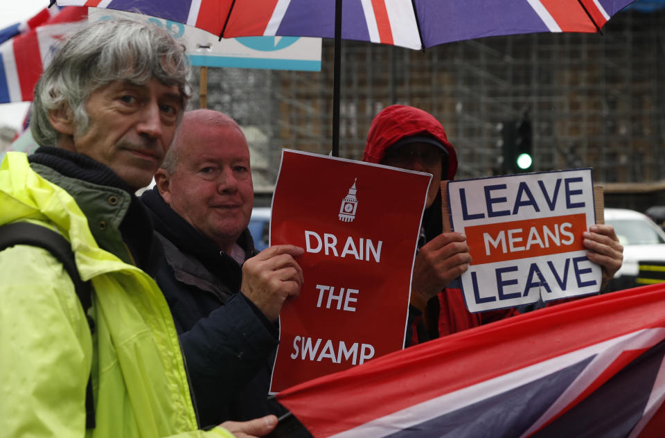 Pro-Brexit protesters hold out their placards and flags as traffic moves past the Houses of Parliament in London, Monday, Oct. 21, 2019. The European Commission says the fact that British Prime Minister Boris Johnson did not sign a letter requesting a three-month extension of the Brexit deadline has no impact on whether it is valid and that the European Union is considering the request. (AP Photo/Alastair Grant)