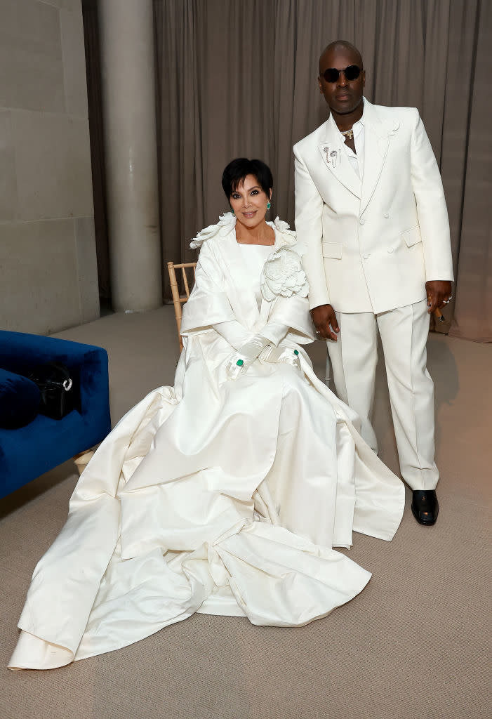 Kris Jenner and Corey Gamble pose together; Kris wears a white origami-inspired gown and Corey in a white suit