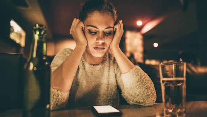 Depressed woman sitting in a bar and looking at her cell phone while waiting for a call from her boyfriend.