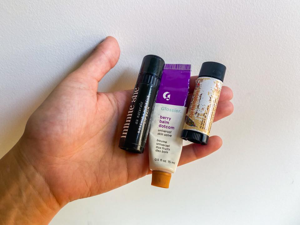 A hand holds three different types of lip balm on a white background