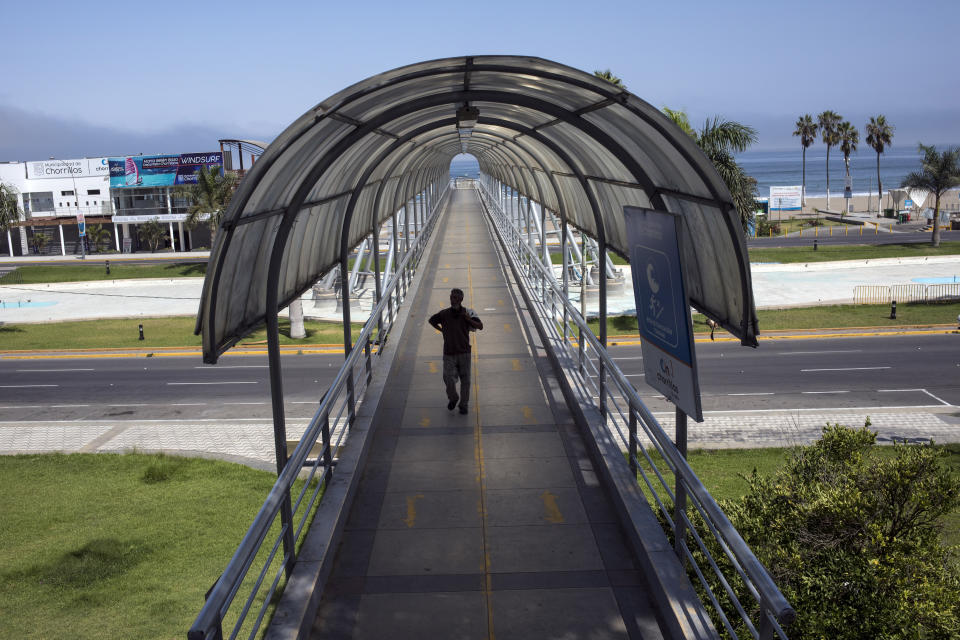 In this March 24, 2020 photo, Cesar Daniel Fiestas crosses a popular pedestrian bridge absent of people, after having a swim in the waters of Agua Dulce beach in Lima, Peru. This year the final days of summer fun came to an abrupt end when Peru's president suspended rights to free movement and instructed people to remain in their homes to help reduce the spread of the new coronavirus. (AP Photo/Rodrigo Abd)