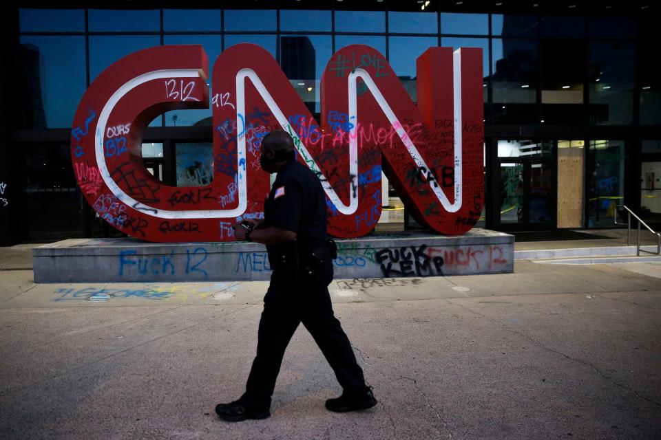 A security guard walks in front of a damaged CNN sign at the CNN Center in the aftermath of a demonstration against police violence on Saturday, May 30, 2020, in Atlanta.