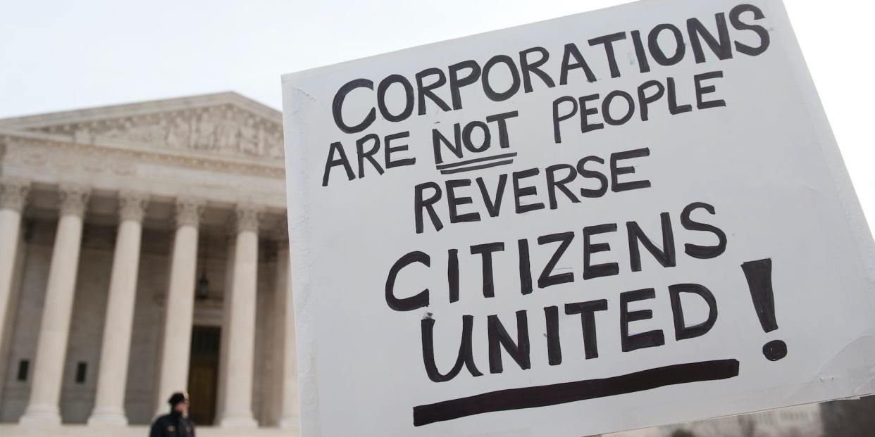 A person holds a sign reading "Corporations are not people, reverse Citizens United!" in front of the Supreme Court