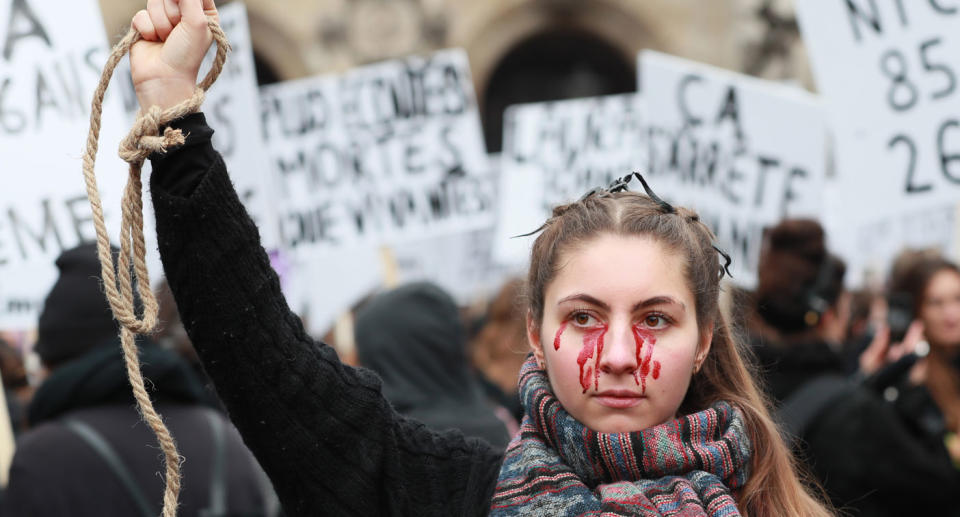 Woman at Paris protest against violence against women with blood-like tears in symbolic pose.