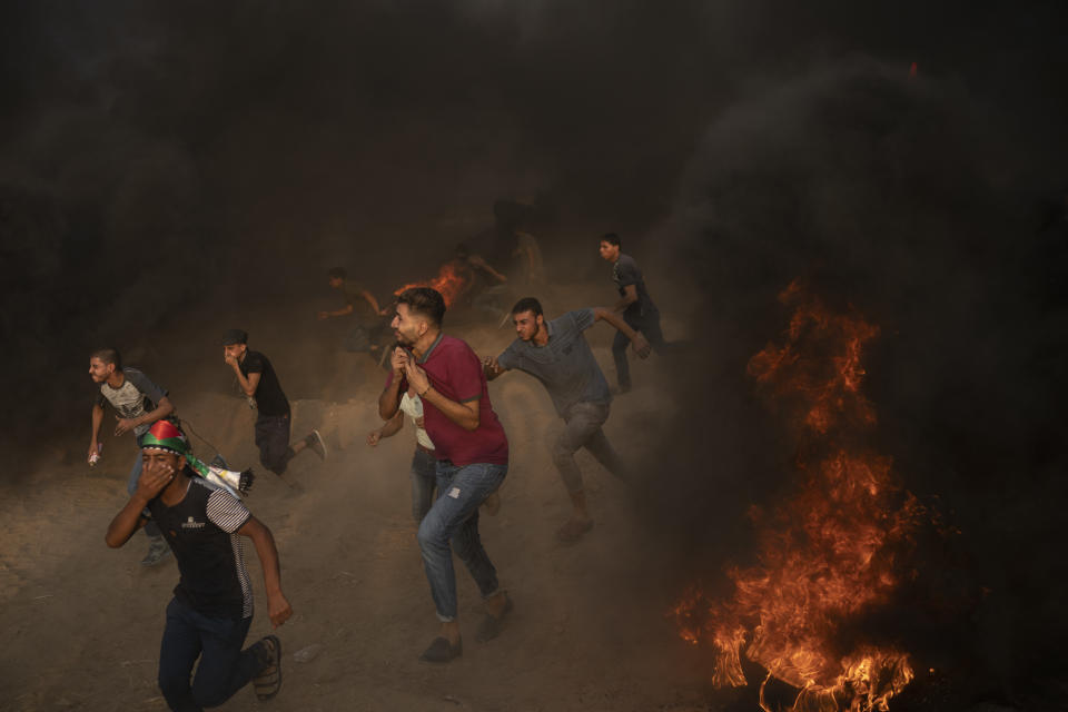 In this Friday, Aug. 31, 2018 photo, Palestinian protesters run from teargas fired by Israeli troops during a protest at the Gaza Strip's border with Israel, east of Gaza City. The 11-year blockade and growing anger have put a lot of pressure on Hamas, which is trying to redirect it toward Israel with relentless protests. (AP Photo/Felipe Dana)