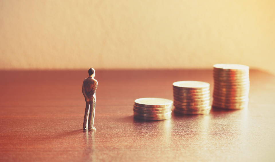 A tiny investor stands in front of stacks of coins.