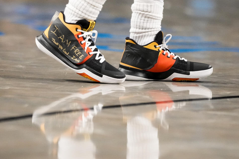 Brooklyn Nets guard Kyrie Irving (11) wears sneakers with logos covered in tape with the words "I AM FREE Thank you God … I AM" written in gold colored marker during the second half of an NBA basketball game against the Charlotte Hornets, Wednesday, Dec. 7, 2022, in New York. (AP Photo/John Minchillo)