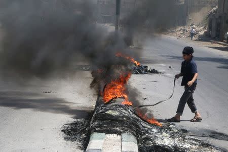 A boy inspects burning tyres, which activists said are used to create smoke cover from warplanes, in Aleppo, Syria August 1, 2016. REUTERS/Abdalrhman Ismail