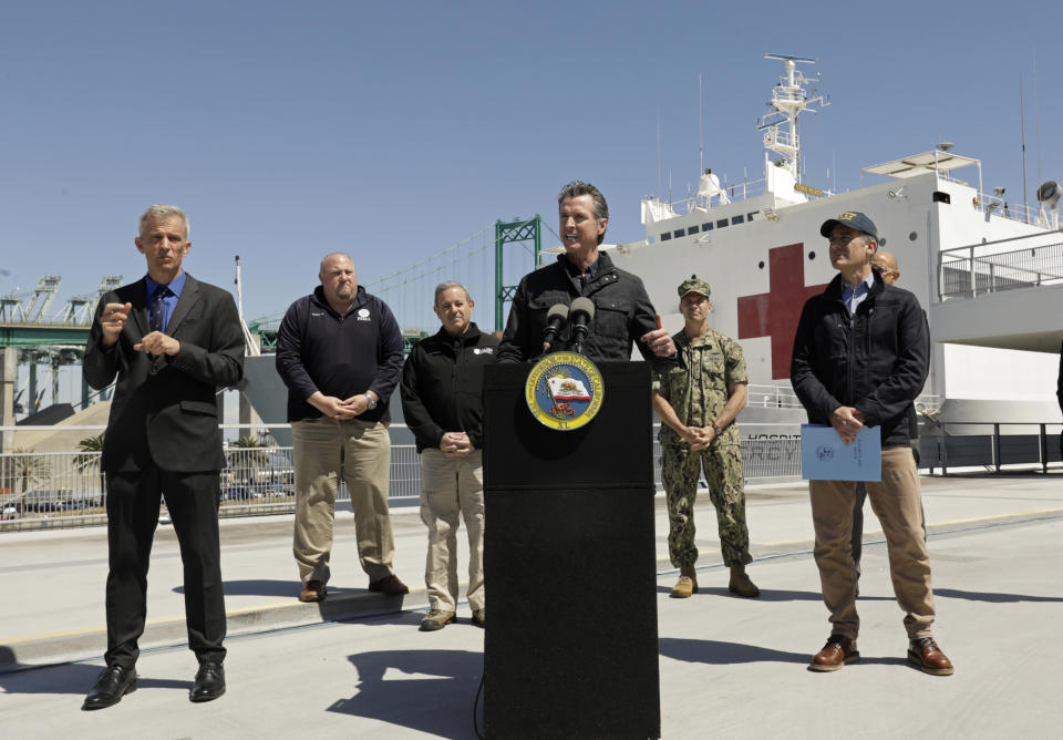 California Governor Gavin Newsom speaks in front of the hospital ship US Naval Ship Mercy that arrived into the Port of Los Angeles on Friday, March 27, 2020, to provide relief for Southland hospitals overwhelmed by the coronavirus pandemic. Also attending the press conference and keeping appropriate distancing are Los Angeles Mayor Eric Garcetti, right, Dr. Mark Ghaly, Secretary of Health and Human Services, behind Garcetti, Director Mark Ghilarducci, Cal OES, third left, Robert Fenton, FEMA Regional Administrator for Region 9, second left, U.S. Navy Admiral John Gumbleton, third right, and interpreter Richard Pope, left. (Carolyn Cole/Los Angeles Times via AP, Pool)