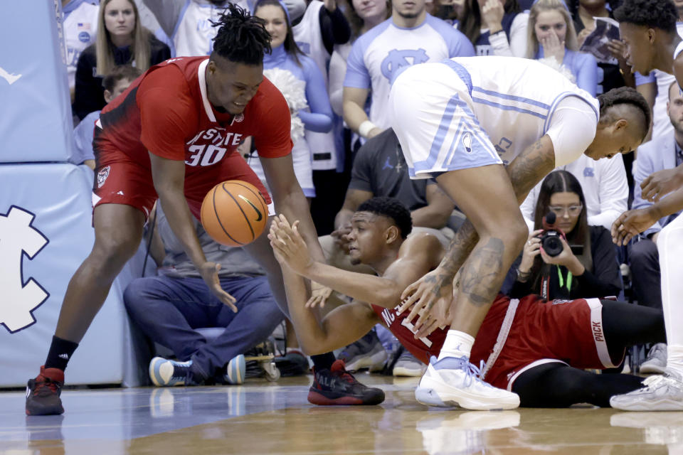 North Carolina State guard Casey Morsell, bottom, passes the ball to forward D.J. Burns Jr. (30) after he got control of the ball against North Carolina forward Armando Bacot, right, during the second half of an NCAA college basketball game Saturday, Jan. 21, 2023, in Chapel Hill, N.C. (AP Photo/Chris Seward)