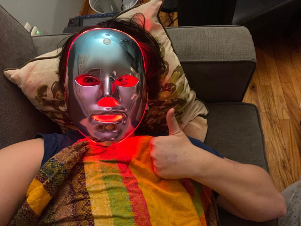 A person lying down with an LED face mask on a couch.