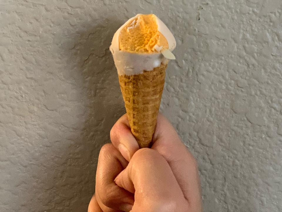 Handing holding Trader Joe's pumpkin hold the cone ice cream in front of a white wall